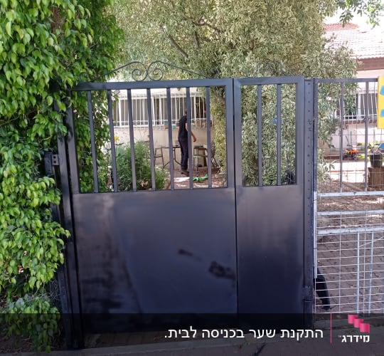 שער מתכת שחור עם סורגים, עץ ברקע